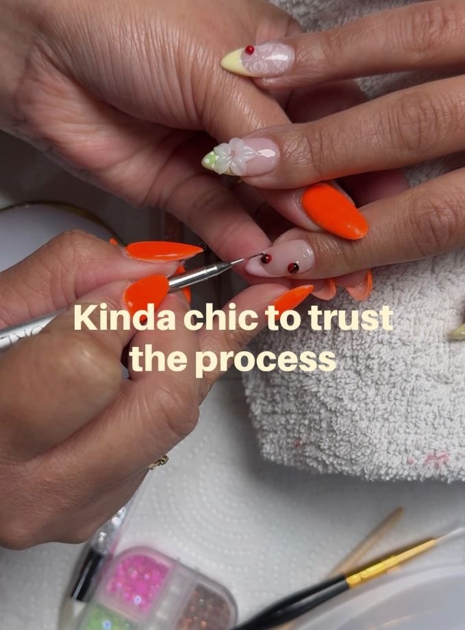 Nail technician painting orange nails with a fine brush